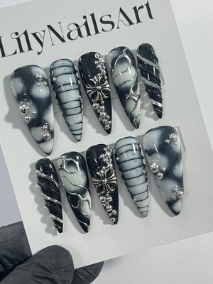 Set of ten black and white press-on nails with silver accents. The nails feature a variety of designs, including swirls, stripes, and a cross.