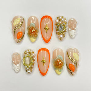 Eight peach-colored nail tips with various designs. The designs include a flower, a star, a heart, and a swirl pattern. The nail tips are decorated with gold and white accents.