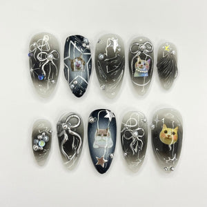 Ten black and white nail art designs featuring cats and stars. Each nail is decorated with a different design, including a cat with a star, a cat with a bow, and a cat with a star on its head.