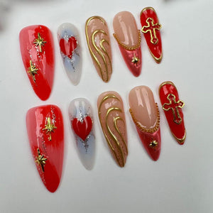 Set of ten false nails with different designs. The designs include a red heart, a gold swirl, a cross, and a star. The nails are all long and pointed.