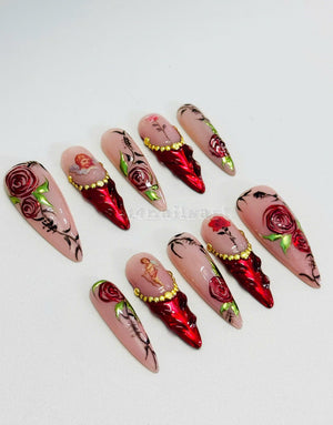 Set of ten long, pointed, false nails with a pink base. Each nail is decorated with a red rose, gold accents, and a cherub image.