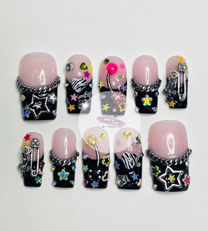 Ten black and pink press-on nails with various colorful designs, including stars, hearts, cherries, and a zebra print. Each nail has a silver chain detail.