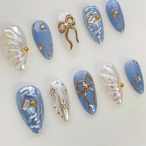 Set of ten blue and white false nails with various designs, including gold bows, stars, and pearl accents.