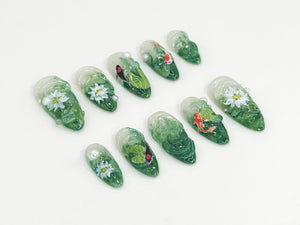 Ten green and white nail art designs featuring flowers, leaves, and fish. The designs are painted on clear nail tips.