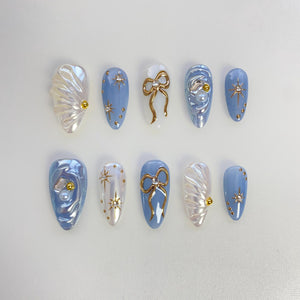 Set of ten blue and white false nails with gold accents. Some nails feature a pearl, a gold bow, or gold stars.
