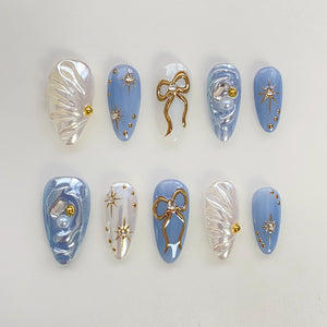 Set of ten blue and white press-on nails with gold accents. The nails feature a variety of designs including bows, stars, and pearl accents.