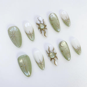 Set of ten green and white almond-shaped press-on nails with gold star and sun designs.
