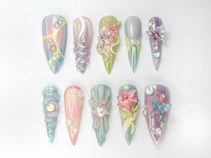 A set of 12 iridescent nail tips with various 3D floral and butterfly designs. The tips are in shades of pink, blue, green, and purple.