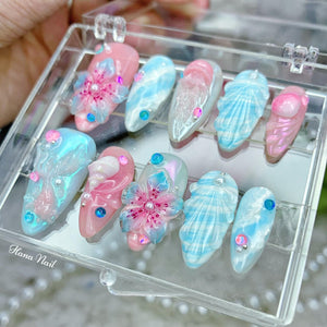 A set of ten fake nails with a beach theme. The nails are decorated with seashells, flowers, and stripes in shades of blue, pink, and white.