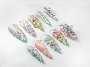 A set of ten iridescent, pastel-colored, long, artificial fingernails with various 3D embellishments, including flowers, seashells, and butterflies.
