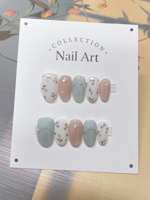 A set of nail art on a white card. The nails are oval-shaped and feature a variety of designs, including solid colors, floral patterns, and silver accents. The card has the text ".COLLECTION. Nail Art