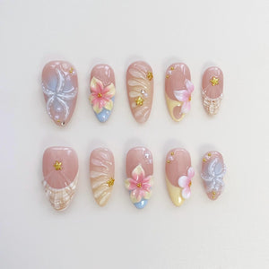 A set of ten artificial nails in various designs. Each nail is a light pink color with detailed floral and abstract designs. Some nails feature 3D flowers in pink, yellow, and blue, while others have