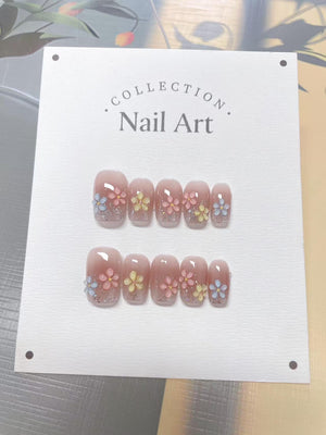 Two sets of artificial nails are displayed on a white card. The nails are a light pink with glitter and small, colorful flower designs. The card has the words "COLLECTION Nail Art" printed on it.