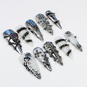 An assortment of silver-toned nail armor, featuring various designs. Some pieces have skull, cross, and floral motifs, while others have a smooth, polished finish. The nail armor is displayed against a white background.