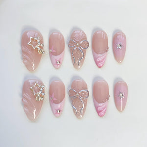 A set of ten artificial nails in various designs. The nails are primarily light pink with accents of silver bows, star-shaped rhinestones, and pink swirls. Some nails feature a French tip design.