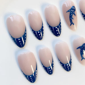 Oval-shaped false nails with a nude base and a navy blue French tip adorned with white polka dots. Some nails feature a navy blue whale shark design. The nails are glossy and appear to be professionally done.