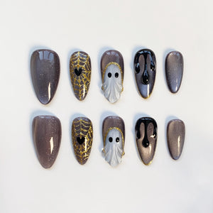 A set of ten Halloween-themed false nails. Designs include glittery gray, gold spiderwebs with black hearts, white ghost figures, and black dripping paint. The nails are almond-shaped and arranged on a white surface.