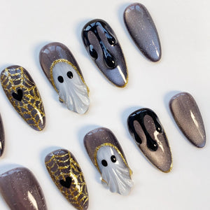 A collection of Halloween-themed nail art designs. The nails feature a variety of designs, including a ghost, spiderwebs with hearts, and dripping black polish. The nails are primarily shades of gray, black, and gold.