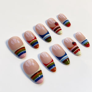 A set of ten artificial nails with a glossy finish. Each nail features a nude base with a French tip and a colorful striped design in shades of red, orange, green, blue, and pink. Some nails have a ladybug accent.