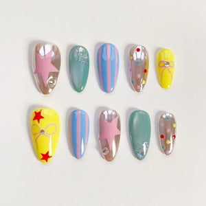 A set of ten artificial nails in various designs. The nails feature a mix of colors, including pink, blue, yellow, and green. Some nails have star, stripe, and dot patterns, while others are solid colors. Each nail is oval-shaped.