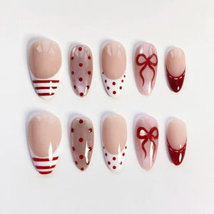A set of ten artificial nails in various designs. The nails feature a nude base with red stripes, polka dots, bows, and French tips. The nails are oval-shaped and arranged on a white surface.