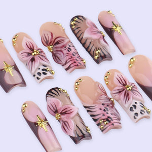 A collection of artificial nails with floral and abstract designs. The nails feature a variety of colors, including pink, brown, and gold. Some nails have a flower design, while others have a leopard print or gold accents.