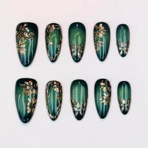Set of ten emerald green press-on nails with gold floral designs. The nails are oval-shaped and feature a glossy finish. The gold accents are applied in various floral patterns, adding a touch of elegance.