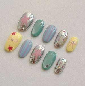 A set of ten artificial nails in various designs. The nails feature a mix of colors including silver, yellow, and teal. Some nails have star and bow designs, while others have stripes and polka dots. Each nail is oval-shaped.