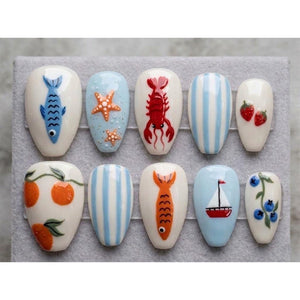 A set of ten artificial nails with various hand-painted designs. The designs include a blue fish, starfish, a red lobster, blue and white stripes, strawberries, oranges, an orange fish, a sailboat, and blueberries.