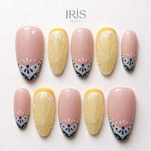 A set of ten artificial nails with a light pink base. Some nails feature a yellow lemon slice design, while others have a white and blue floral pattern at the base. The brand name "IRIS NAILART" is in the top left corner.