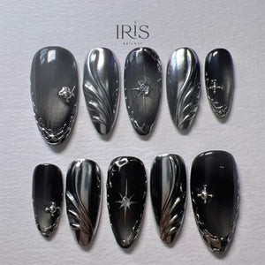 A set of ten press-on nails in a dark gray and silver color scheme. The nails feature intricate silver designs, including floral patterns, starbursts, and decorative edges. The brand name "IRIS NAILART" is visible at the top.