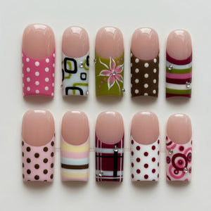 A set of ten artificial nails with various designs. The nails feature a natural pink tip and a range of patterns, including polka dots, geometric shapes, floral designs, and stripes. Some nails have decorative rhinestones.