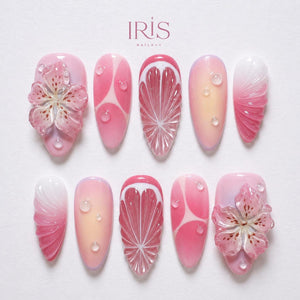 A set of ten pink and white acrylic nails with various designs. Some nails feature a 3D flower, others have a citrus fruit design, and some have water droplet accents. The brand name "IRIS NAILART" is at the top.