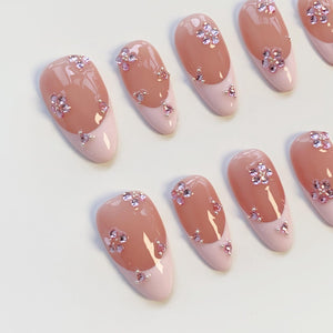 A set of artificial nails with a French manicure design. The nails feature a light pink base with a darker pink tip. Each nail is adorned with pink flower-shaped rhinestones, adding a touch of sparkle and elegance to the overall look.