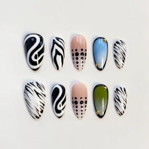 A set of ten artificial nails in various designs. The nails feature patterns including black and white swirls, zebra stripes, and dotted designs. Some nails have a solid color, including pink, blue, and green, with gold accents.