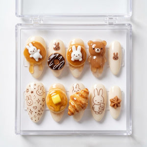 A set of ten artificial nails with various food and animal-themed designs. The nails feature a bunny, bear, donut, pancake, and croissant. The nails are in a clear plastic case.
