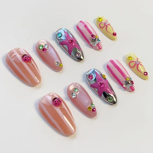 A collection of artificial nails in various designs. Some nails are pink with white stripes or ladybug accents. Others feature silver chrome with pink stars, or pink and white stripes with star and gem embellishments. Some are yellow with pink bows.