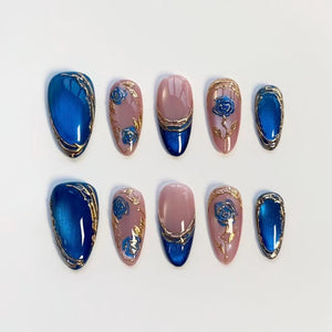 A set of ten artificial nails in various sizes. The nails feature a glossy blue, pink, and gold design. Some nails have a blue rose design, while others have a solid blue or pink base with gold accents.