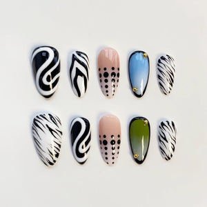 A set of ten artificial nails in various designs. The nails feature patterns like black and white swirls, zebra stripes, and dotted designs. Some nails have a gradient of color, and some have small gold accents.