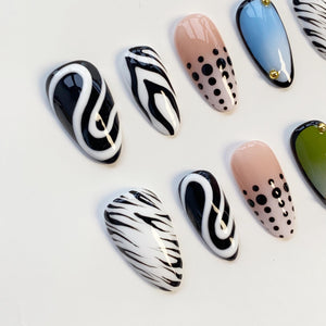 A collection of artificial nails with various designs. Some nails feature black and white swirls, others have zebra stripes, and some are painted with a nude base and black polka dots. A few nails have a blue or green gradient.