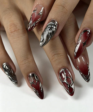 Long almond-shaped nails featuring a deep red gradient base color. The nails are decorated with raised, reflective silver metallic liquid-style accents that form intricate, organic, and flowing patterns across the surface of each nail.