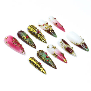 A set of ten stiletto-shaped press-on nails featuring a variety of designs including red and white gradients, metallic gold accents, embedded red rhinestones, small white pearls, and gold cross charms arranged on a plain white surface.
