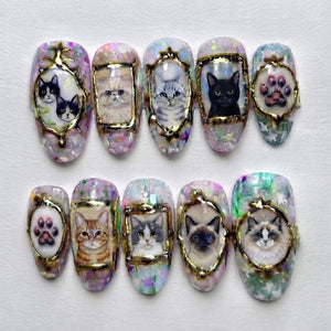 A set of ten press-on nails featuring hand-painted cat portraits and paw prints encased in gold-toned frames. The background of each nail displays a multi-colored, iridescent, and glittery finish with various feline breeds depicted.