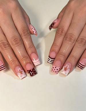 Square-shaped fingernails featuring a French manicure style with a mix of designs. Some nails have dark maroon tips with white polka dots, others have light pink stripes, and some feature a hand-painted white flower with pink accents.