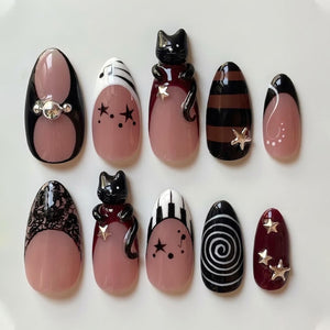 A set of ten press-on nails featuring a nude base with various designs including black cat figures, silver star charms, piano keys, musical notes, black lace patterns, brown and black stripes, and a white spiral on a black background.