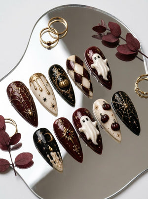 A set of ten almond-shaped press-on nails featuring intricate Halloween-themed designs in black, cream, and deep burgundy. Details include raised white ghosts, gold spiderwebs, pumpkins, stars, moons, candles, and harlequin patterns.