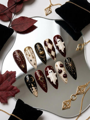 A set of ten stiletto-shaped press-on nails featuring Halloween-themed designs. The nails display intricate details including raised white ghosts, gold spiderwebs, black and gold pumpkins, stars, moons, and a cream-colored drip pattern.