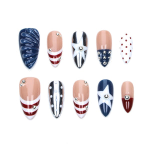 A set of ten almond-shaped press-on nails featuring patriotic designs in red, white, and blue. The collection includes textured navy blue, striped patterns, white stars, silver metallic accents, red polka dots, and small silver studs.