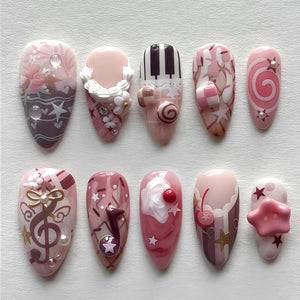 A set of ten almond-shaped press-on nails featuring a pink and brown color palette. Designs include piano keys, a treble clef, musical notes, cherries, stars, swirls, and three-dimensional accents like flowers and a pink star.