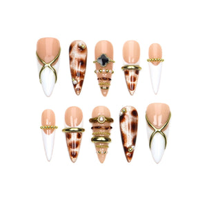 A set of ten stiletto-shaped press-on nails featuring a mix of nude and white bases. Designs include leopard print patterns, gold metallic cross overlays, small pearl accents, and stacked gold-toned rings across the nail surfaces.